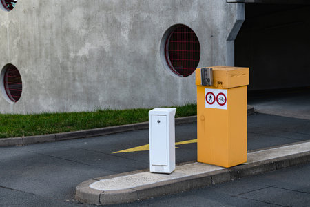 Two box stand on the side of a street in a parking area. One is yellow with signs, and the other is...