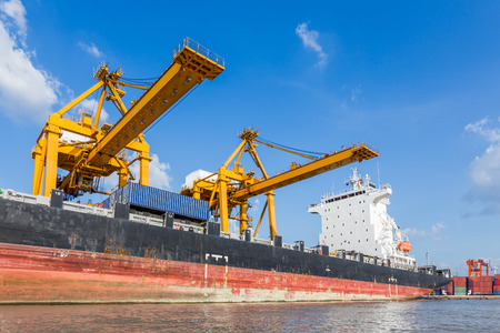 Container cargo freight ship with working crane loading bridge in shipyard for logistic Import export backgroundの写真素材