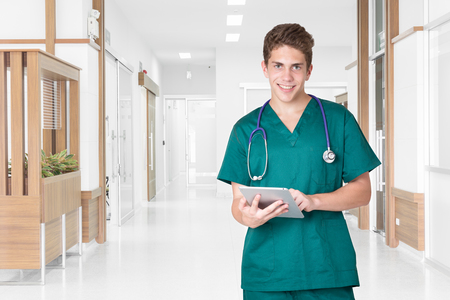 Smiling young doctor using tablet in hospital hallwayの写真素材