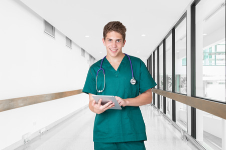 Smiling young doctor using tablet in hospital hallwayの写真素材