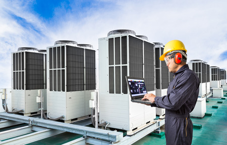 Electrical engineer using laptop computer for maintenance air conditioning system on rooftop of factoryの写真素材