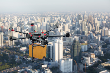 Drone transport  flying with cardboard box above city, futuristic delivery conceptの写真素材