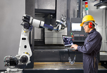 Maintenance engineer using laptop computer control automatic robotic hand with CNC machine in smart...