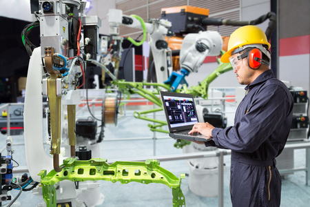 Engineer using laptop computer maintenance automatic robotic hand machine tool in automotive industry, Smart factory conceptの写真素材