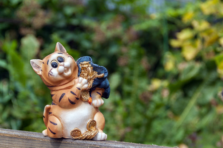 Figurine of a cheerful tiger with a bag of money. Garden in the background