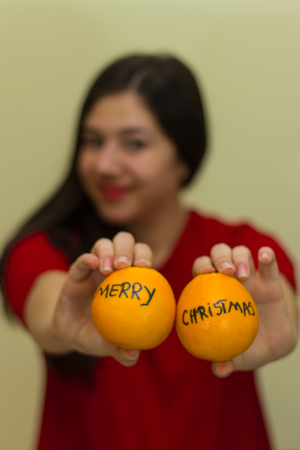 Out of focus girl holding 2 oranges with "Merry Christmas" written on themの写真素材