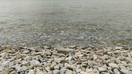The beach with colorful pebbles and a bustling ocean. Backgroundの写真素材