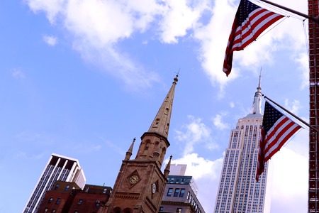American flag flying in the wind against a blue sky and skyscrapersの写真素材