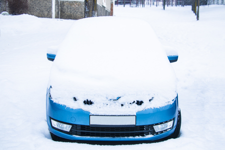 Frozen car covered snow at winter day, view front window windshield and hood on snowy backgroundの写真素材