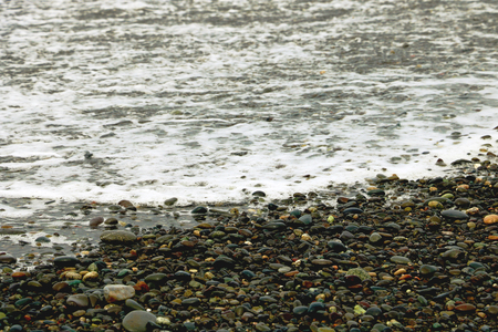 Pebble stones on the beach, the rolling waves of the sea with foamの写真素材