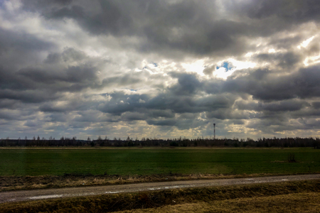 Green field against the dark sky, the sun through the cloudsの写真素材