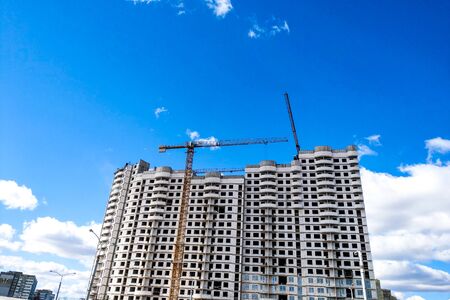 View of the construction cranes and the new house under construction against the blue skyの写真素材