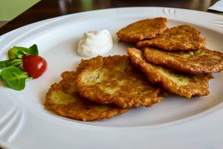 Delicious homemade potato pancakes on plate with sour cream