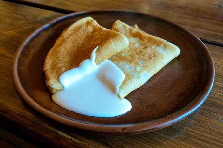 Pancakes on a plate with sour cream. Traditional for the Russian pancake week. Dark backgroundの写真素材