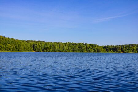 View of a blue lake or river on a sunny day on a background of blue sky and green forestの写真素材