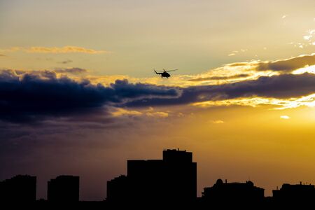A helicopter flies over the city in the evening during sunsetの写真素材