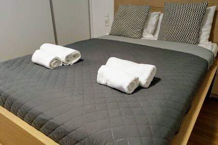 View of the made-up bed with pillows in the bedroom with towels on itの写真素材