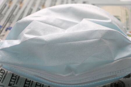 Medical mask laying on dollars, concept of increasing costs for protection of virus like the coronavirus or Covid19の写真素材