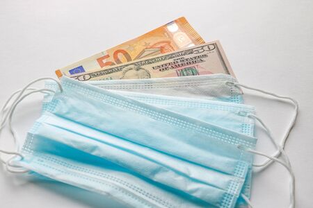 Medical mask on euro banknotes and dollars. The concept of increasing the price of protecting the respiratory tract from the virus. Dependence of world currencies and the economy as a whole on epidemicsの写真素材
