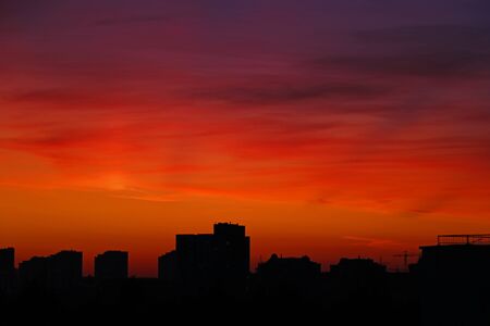 Bright orange sunset over the city in the evening. Bright lights of high-rise buildings of urban buildings. Silhouette of construction city crane of building under construction, selective focusの写真素材