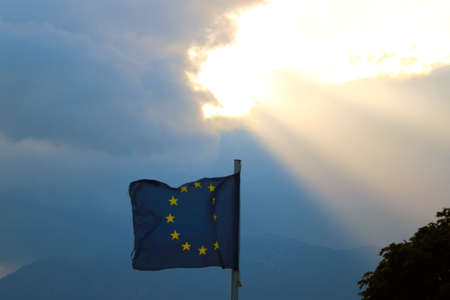 The flag of the european union flies in the wind against the backdrop of mountains at sunsetの写真素材