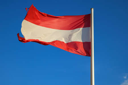 The Austrian flag flutters in the wind against the blue skyの写真素材