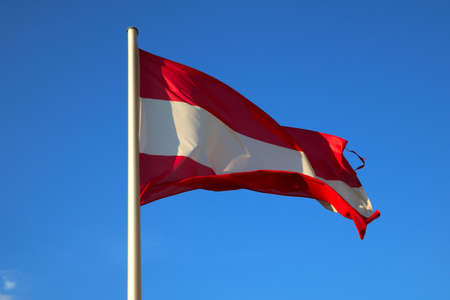 The Austrian flag flutters in the wind against the blue skyの写真素材