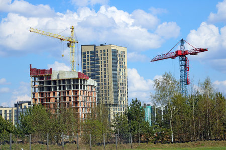 View of construction cranes and building modern houses against a blue sky with white cloudsの写真素材