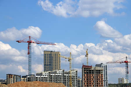 Construction cranes and houses under construction against the skyの写真素材