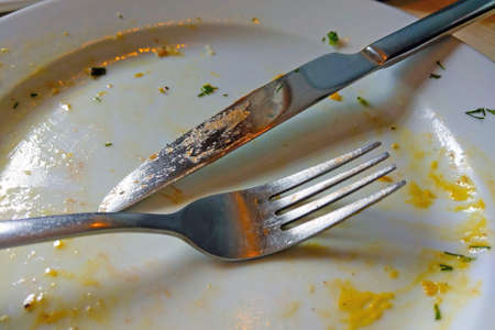 Fork and knife on a white plate after eatingの写真素材