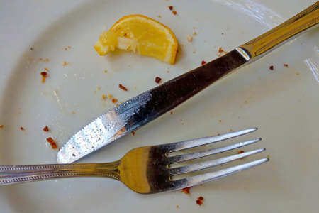 Dirty white plate with fork and knife after eating