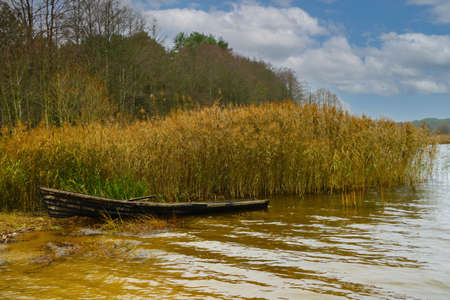 On the shore of the lake near the bushes there is a wooden boatの写真素材