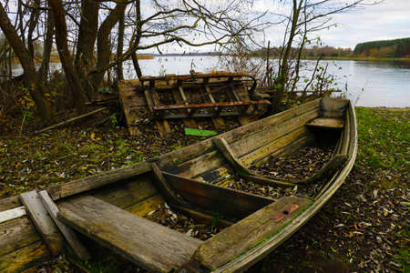 An old wooden wrecked boat on the shore of the lake in the fallの写真素材