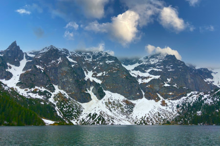 Picturesque view of a mountain lake with rocks of snow against the blue sky.の写真素材