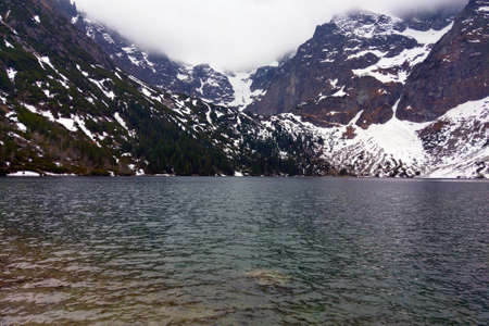 View of the lake and mountains with snow on a foggy morningの写真素材