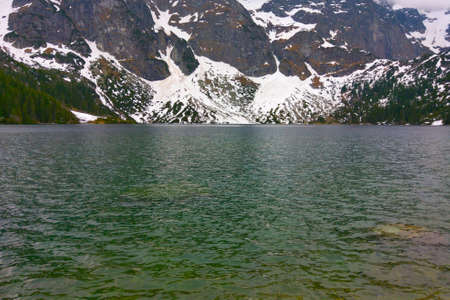 View of the lake against the backdrop of the mountain on a cloudy dayの写真素材