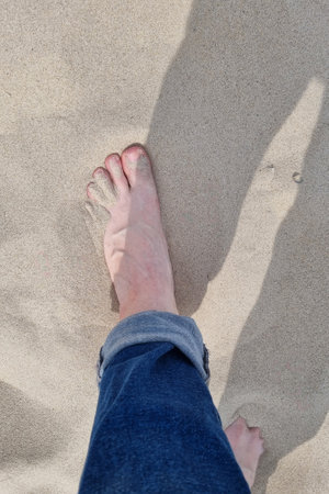 View of the foot of a man resting in the sand on the beach near the sea or ocean. Warm beach sand,...
