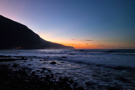 A picturesque sunset on the beach or ocean. Waves roll onto the beach. Rocky coast during sunsetの写真素材