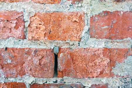 An up-close view of a weathered brick wall with a noticeable hole in the center. The rough texture...