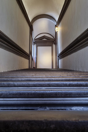 A view up a historic stone staircase leading to an arched doorway. the narrow hallway is framed by smooth, light-colored walls and elegant molding, illuminated by warm artificial light. a timeless architectural detail ideal for designs focused on classic and historical themes.の写真素材