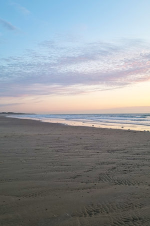 A serene early morning beach scene featuring soft ocean waves under a pastel-colored sky. the...