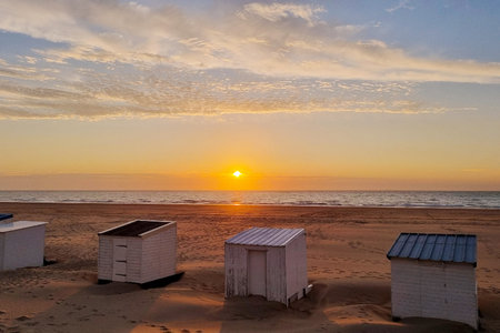 Stunning sunset over a serene beach featuring white seaside cabins. the sun sets on the horizon, casting a warm glow and reflections over the gentle waves and sandy shore, perfect for travel, vacation, and relaxation themes.の写真素材