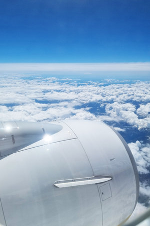 Mid-flight view of a bright blue sky filled with fluffy white clouds, as seen from an aircraft window. the airplane's engine is prominently visible, symbolizing travel, adventure, and the joy of flying above the earth.の写真素材