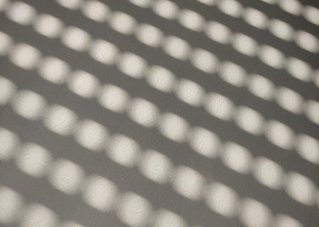 Repetition of circular shadows creates a geometric pattern on a white textured surface. the interplay of light and shadow forms an abstract design, ideal for artistic backgrounds or modern decor concepts.の写真素材