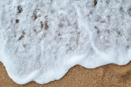 A detailed view of gentle ocean waves washing over sandy beach, creating a calming and serene coastal scene. ideal for themes of relaxation, nature, and tranquility, perfect for summer or vacation designs.の写真素材