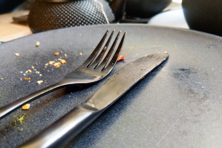 A close-up of a dark plate with a fork and knife resting on it, surrounded by crumbs, symbolizing the completion of a meal. the image conveys themes of dining, culinary experiences, and the aftermath of enjoying food.の写真素材