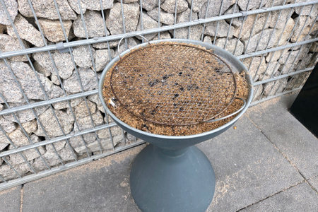 Outdoor barbecue grill covered with ash and residue, set against a rustic stone wall. ideal for...