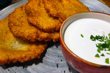Crispy golden potato pancakes served alongside a bowl of creamy sour cream garnished with fresh...