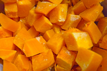 Close-up of vibrant, freshly cut pumpkin cubes showcasing their vivid orange color and texture. ideal for cooking, fall recipes, thanksgiving preparations, and healthy meal inspirations.の写真素材