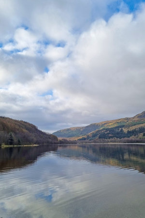 Tranquil autumn landscape featuring a serene lake with clouds reflecting on the water surface....
